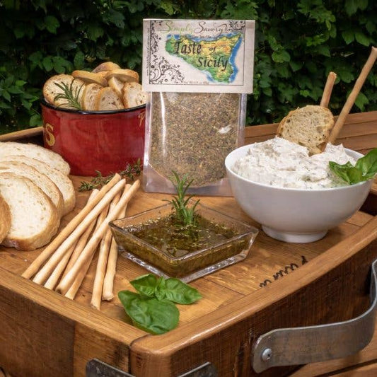 Simply Savory Taste of Sicily Dip Mix displayed with a creamy dip, crusty bread, breadsticks, and fresh basil on a wooden tray